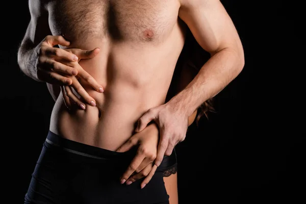 Partial view of female hands touching man with shirtless torso isolated on black — Stock Photo