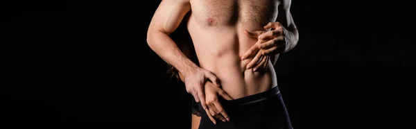 Partial view of female hands touching man with shirtless torso isolated on black, banner — Stock Photo