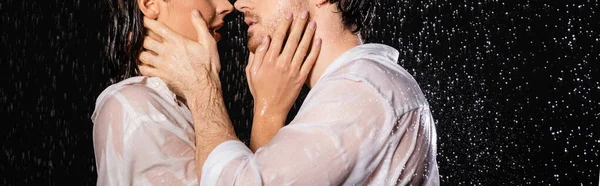 Vista recortada de pareja sexy apasionada en ropa mojada besándose en gotas de lluvia sobre fondo negro, pancarta - foto de stock