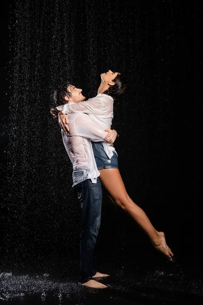 Мокрая счастливая и страстная романтическая пара обнимающая капли дождя на черном фоне — стоковое фото