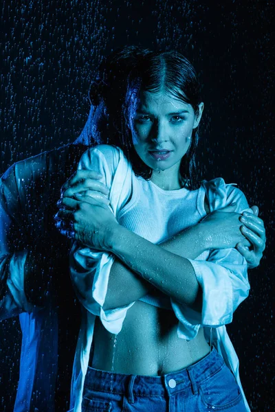 Homem gentilmente abraçando mulher sedutora sexy em gotas de água no fundo preto com filtro de cor azul — Fotografia de Stock