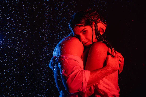 Red and blue colors filters picture of wet passionate romantic couple gently hugging in water drops on black background — Stock Photo