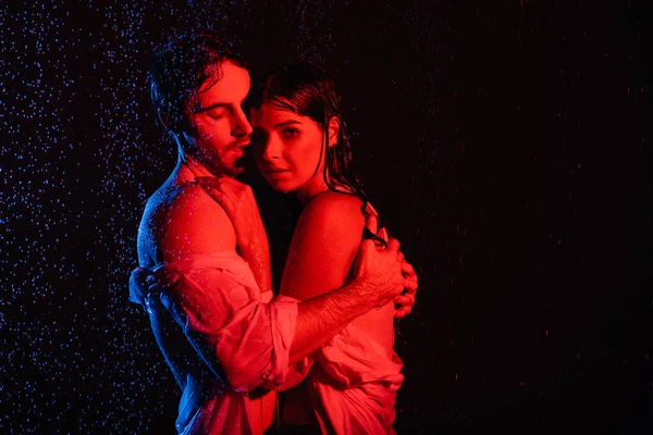 Red and blue colors filters picture of wet passionate romantic couple hugging in water drops on black background — Stock Photo