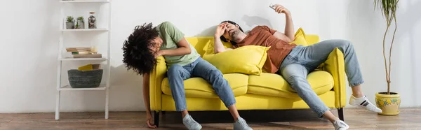 Jovem casal interracial sofrendo de calor no sofá amarelo, banner — Fotografia de Stock