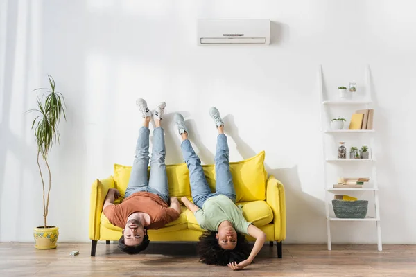 Jovem casal interracial sofrendo de calor no sofá amarelo na sala de estar moderna — Fotografia de Stock