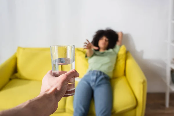 Blurred african american woman with outstretched hand reaching glass of water in male hand — Stock Photo
