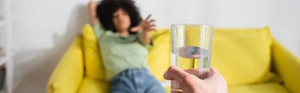 Mujer afroamericana borrosa con la mano extendida que alcanza el vaso de agua en la mano masculina, bandera - foto de stock