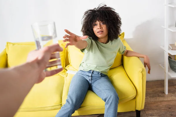 Afroamerikanerin mit ausgestreckter Hand, die in verschwommener männlicher Hand nach einem Glas Wasser greift — Stockfoto