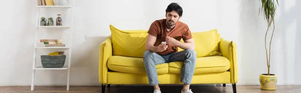 Hombre sosteniendo mando a distancia mientras que sufre de calor en la sala de estar, pancarta - foto de stock