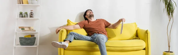 Mann hält Zeitung auf gelbem Sofa und leidet unter Hitze im Wohnzimmer, Transparent — Stockfoto