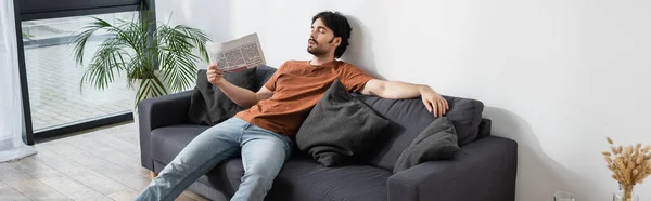 Man waving with newspaper while lying on gray sofa and suffering from heat, banner — Stock Photo