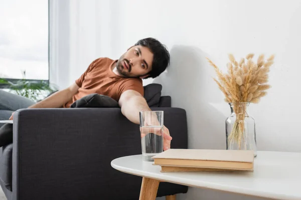 Homme atteignant un verre d'eau sur une table basse floue tout en souffrant de chaleur — Photo de stock