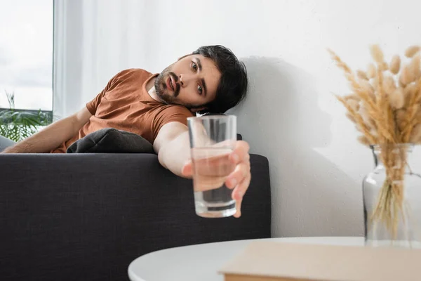 Bearded man reaching glass of water on blurred coffee table while suffering from heat — Stock Photo