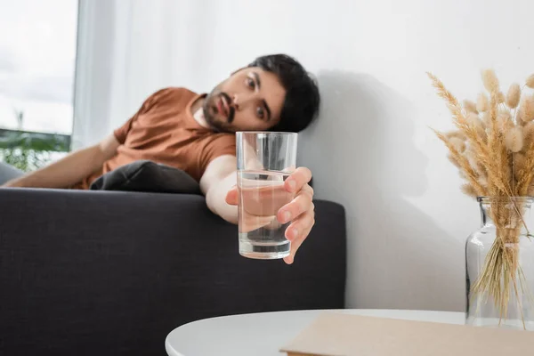 Hombre borroso que alcanza el vaso de agua cerca de la mesa de café mientras sufre de calor - foto de stock