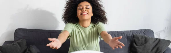 Радостная африканская американка, сидящая с протянутыми руками на диване, баннер — стоковое фото