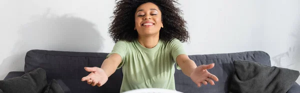 Alegre mujer afroamericana sentada con las manos extendidas en el sofá, pancarta - foto de stock