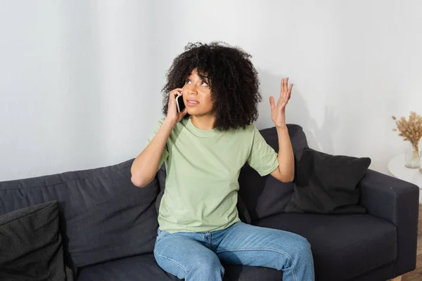 Unzufriedene Afroamerikanerin spricht im Wohnzimmer auf Smartphone — Stockfoto