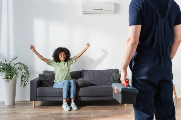 Rizado africano americano mujer regocijo cerca handyman con caja de herramientas - foto de stock