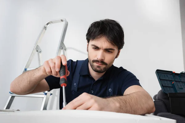 Bearded handyman in overalls holding screwdriver while fixing broken air conditioner — Stock Photo