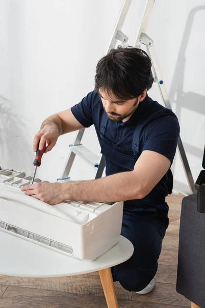 Handwerker in Overalls hält Schraubenzieher, während er kaputte Klimaanlage repariert — Stockfoto