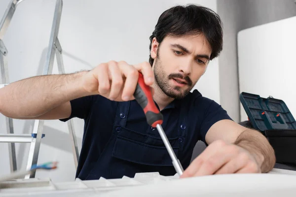 Konzentrierter Heimwerker in Overalls hält Schraubenzieher während er kaputte Klimaanlage repariert — Stockfoto