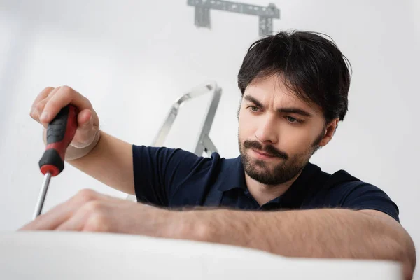 Concentrated handyman holding screwdriver while fixing broken air conditioner — Stock Photo