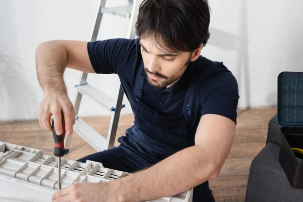 Bearded handyman holding screwdriver while fixing broken air conditioner — Stock Photo