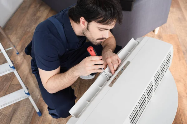 High angle view of bearded handyman holding screwdriver while fixing broken air conditioner — Stock Photo