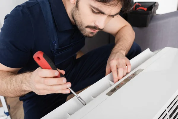 Bärtiger Handwerker mit Schraubenzieher bei der Reparatur moderner Klimaanlage — Stockfoto