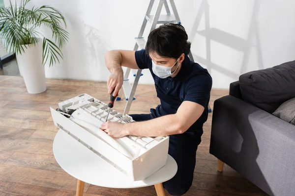 Handwerker in medizinischer Maske hält Schraubenzieher während er defekte Klimaanlage repariert — Stockfoto