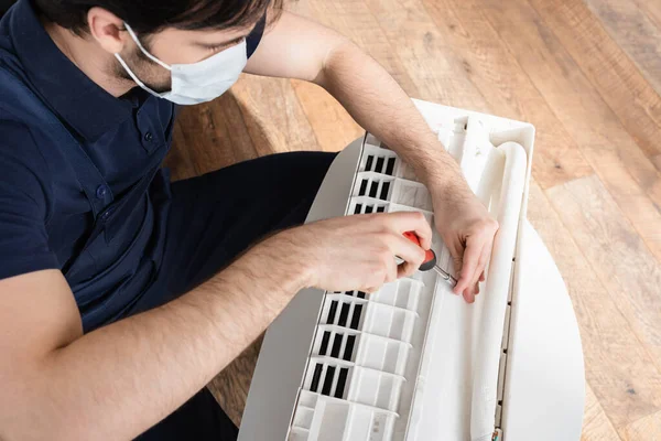 High angle view of handyman in medical mask fixing broken air conditioner — Stock Photo