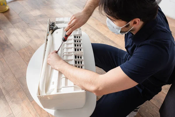 Handyman in medical mask fixing broken air conditioner — Stock Photo