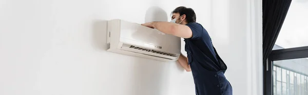 Repairman in medical mask fixing air conditioner, banner — Stock Photo