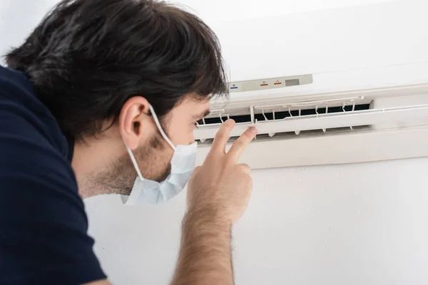 Handyman in medical mask gesturing near air conditioner while checking climate control — Stock Photo