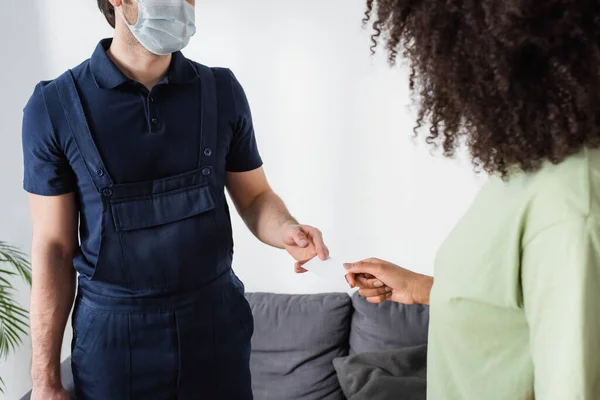 Partial view of handyman in medical mask giving blank card to curly african american woman — Stock Photo