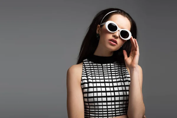 Молода жінка в обкладинці, що регулює білі сонцезахисні окуляри ізольовані на сірому — стокове фото