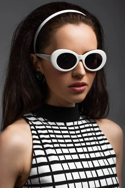 Mujer joven en diadema y gafas de sol con estilo aislado en gris - foto de stock