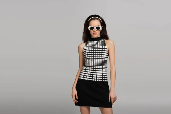 Модна молода модель в сонцезахисних окулярах, пов'язці для голови і ретро вбрання ізольована на сірому — стокове фото