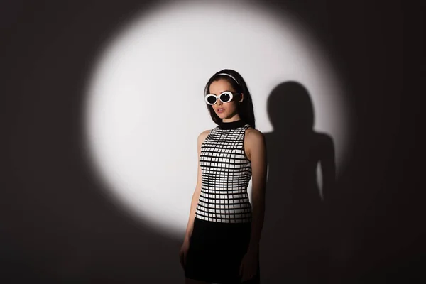 Iluminação no modelo elegante em óculos de sol posando em cinza — Fotografia de Stock