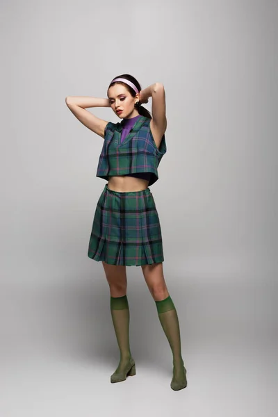 Longitud completa de la mujer joven con estilo en diadema y traje a cuadros posando en gris - foto de stock