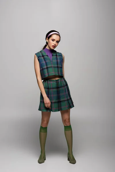 Full length of young woman in headband and checkered outfit posing on grey — Stock Photo