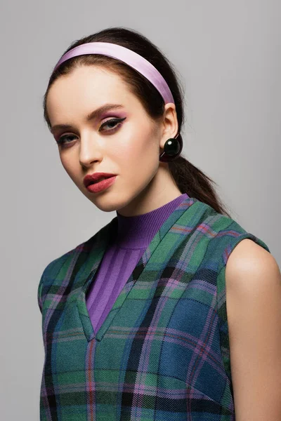 Hübsche junge Frau mit lila Stirnband und Ohrring, die isoliert auf grau in die Kamera blickt — Stockfoto