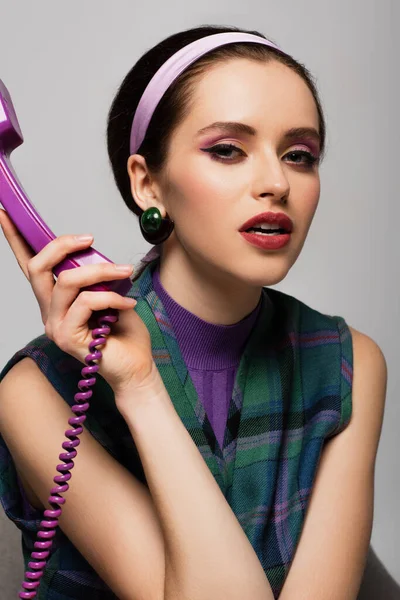 Brünette junge Frau hält lila Retro-Handy isoliert auf grau — Stockfoto