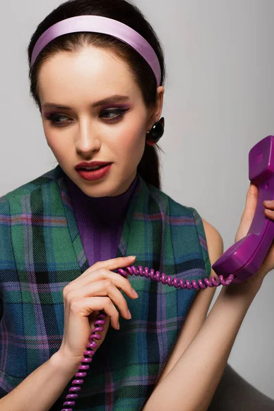 Bonita mujer joven sosteniendo púrpura teléfono retro aislado en gris - foto de stock