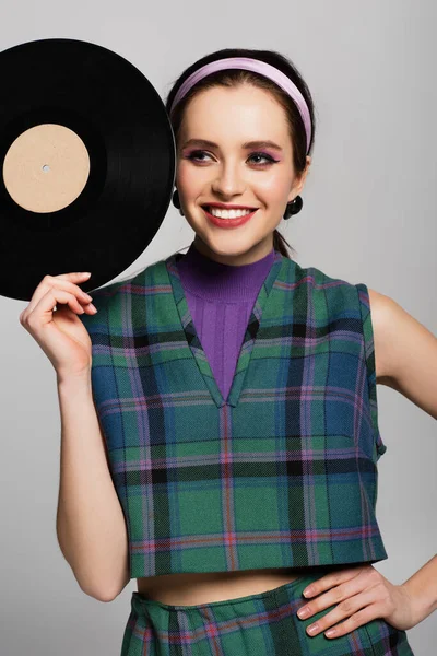 Smiling woman in retro outfit holding retro vinyl disc isolated on grey — Stock Photo