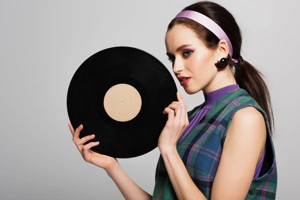 Pretty young woman in headband holding retro vinyl disc isolated on grey — Stock Photo