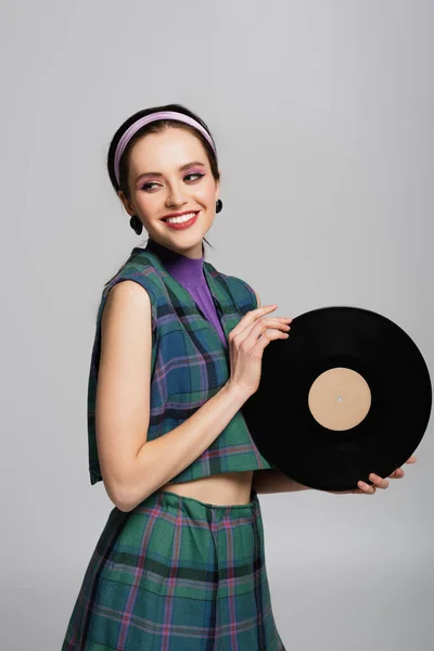 Happy young woman in headband holding retro vinyl disc isolated on grey — Stock Photo