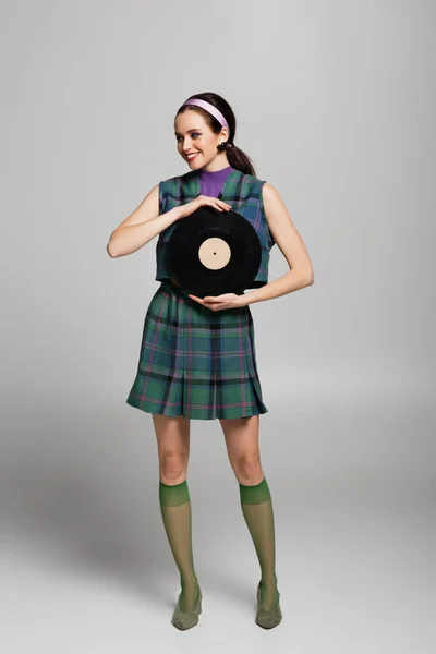 Pleine longueur de jeune femme heureuse dans le bandeau tenant disque de vinyle rétro sur gris — Photo de stock