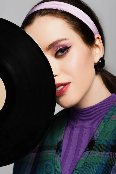 Young woman in headband looking at camera near retro vinyl disc isolated on grey — Stock Photo