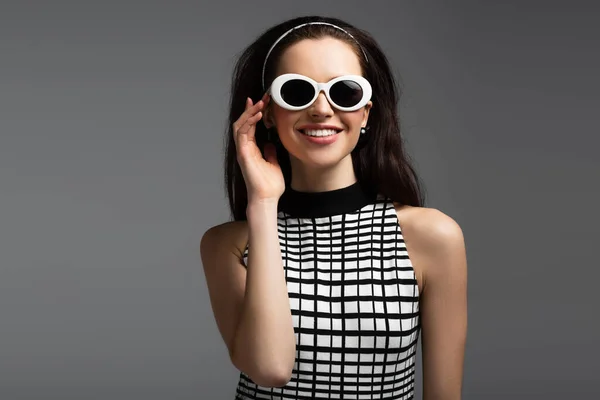Весела молода жінка регулює сонцезахисні окуляри ізольовані на сірому — стокове фото